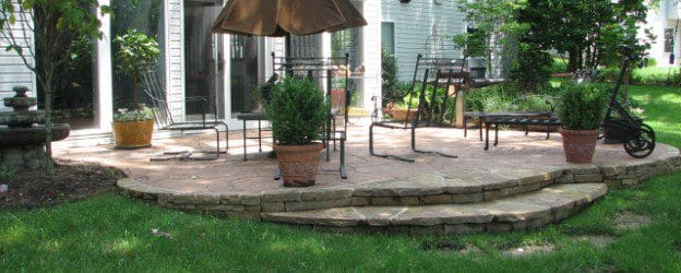 A brick patio with an umbrella and chairs.