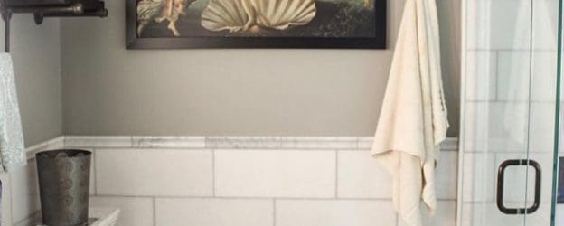 A bathroom with white tile and a picture hanging above the shower.